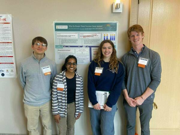 4 BRAIN Lab undergraduate research assistants standing in front of their poster at the Neuroscience Impact Summit.