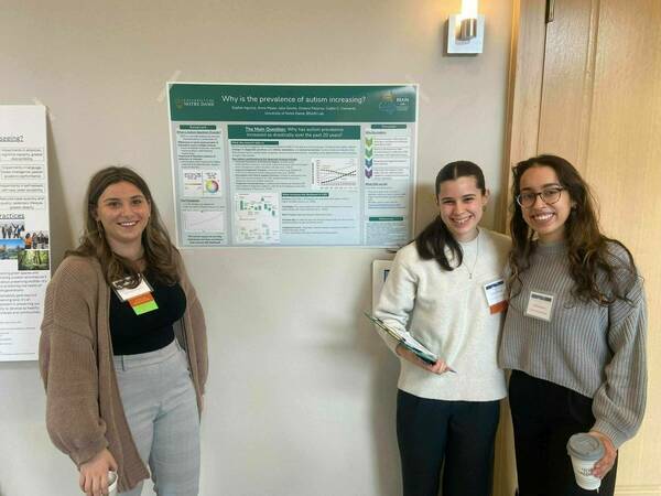 3 BRAIN Lab undergraduate research assistants standing in front of their poster at the Neuroscience Impact Summit.