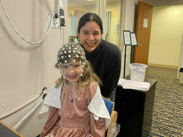 BRAIN Lab research assistant smiling with a child wearung an EEG cap.